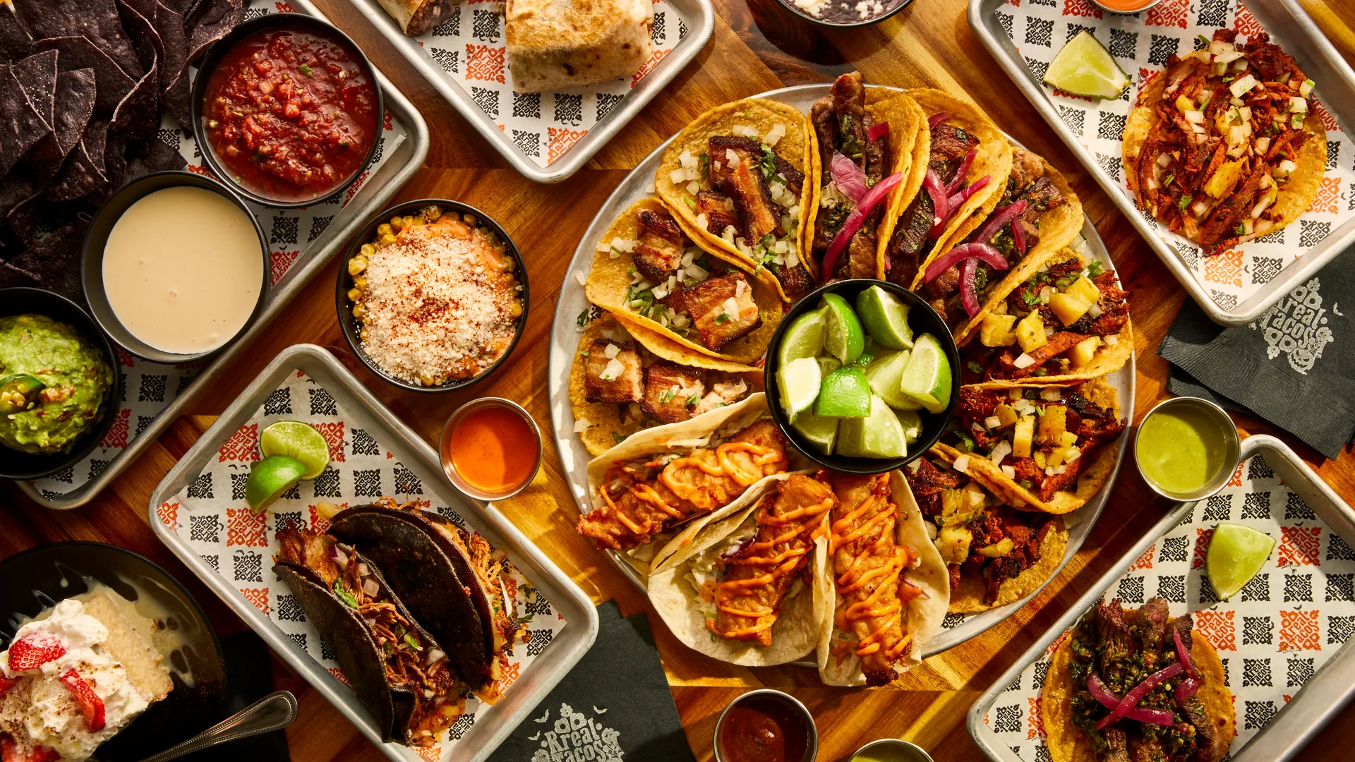 Rreal Tacos spread — a platter of tacos, burritos, chips, salsas, guacamole and street corn on trays